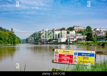 Vista dall'alta marea lungo il fiume Avon, Bristol, Regno Unito, verso il ponte sospeso di Clifton. Un segnale avverte di pericolose correnti fluviali e di non nuotare Foto Stock