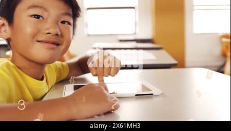 Immagine di più numeri da vicino di un ragazzo asiatico sorridente che usa un tablet digitale in classe Foto Stock