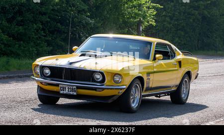 Stoke Goldington, Regno Unito - 12 maggio 2024: 1969 auto d'epoca Ford Mustang gialla che guida su una strada britannica Foto Stock