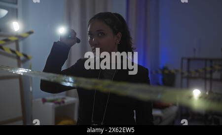 Una giovane donna ispanica indaga su una scena del crimine al chiuso tenendo in mano una torcia, ritraendo un'espressione intensa e concentrata. Foto Stock