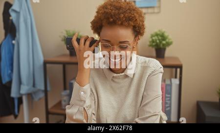 Una donna afroamericana gioiosa ama una conversazione telefonica nel suo elegante soggiorno. Foto Stock