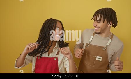 Una donna e un uomo gioiosi in grembiuli che ballano insieme su uno sfondo giallo, ritraendo una vivace scena interna. Foto Stock