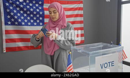 Una giovane donna in un hijab che usa uno smartphone con una bandiera americana e una casella di voto indica un impegno elettorale. Foto Stock