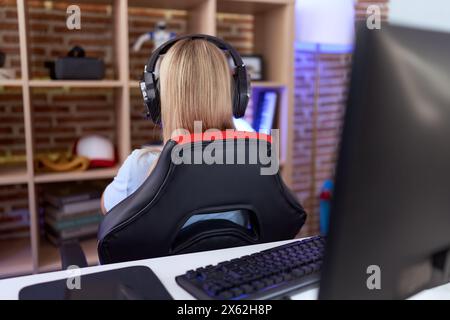 Giovane donna caucasica che gioca ai videogiochi indossando le cuffie in piedi all'indietro guardando lontano con le braccia incrociate Foto Stock