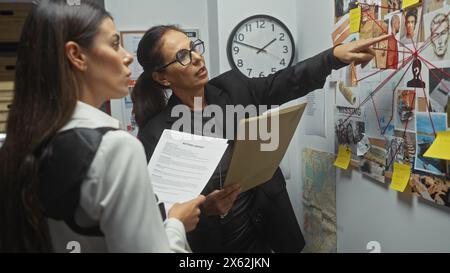 Due detective donne analizzano le prove su una bacheca nella sala investigativa di un dipartimento di polizia. Foto Stock