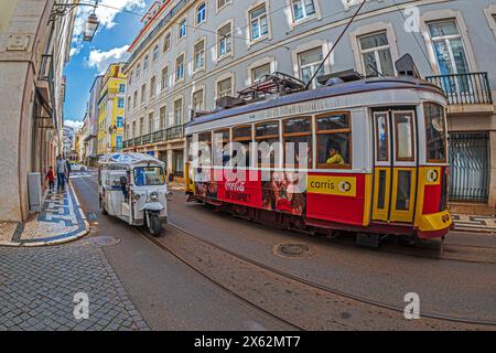 LISBONA, PORTOGALLO - 8 APRILE 2024: Trasporto turistico con divertente auto elettrica chiamata Tuk Tuk e tram d'epoca per le strade della città. Foto Stock