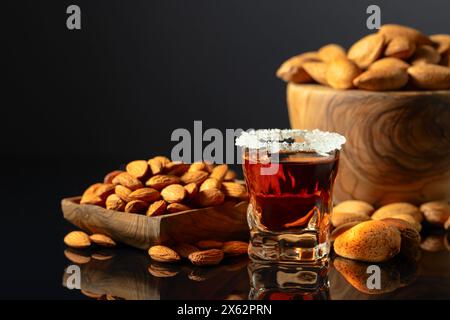 Liquore italiano alcolico forte Amaretto con noci di mandorle su fondo nero. Foto Stock