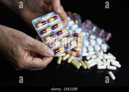 Pillole in mani rugose di anziane donne su sfondo di droga sparso. Farmaco in capsule, assunzione di sedativi, antibiotici o vitamine in età avanzata Foto Stock