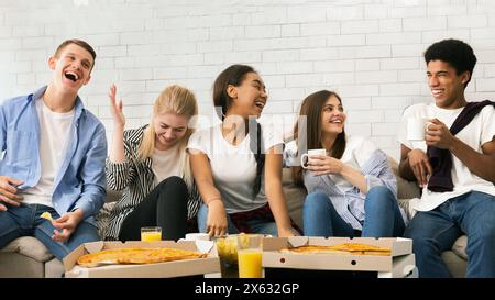 Gruppo di adolescenti che ridono e mangiano la pizza su un divano Foto Stock