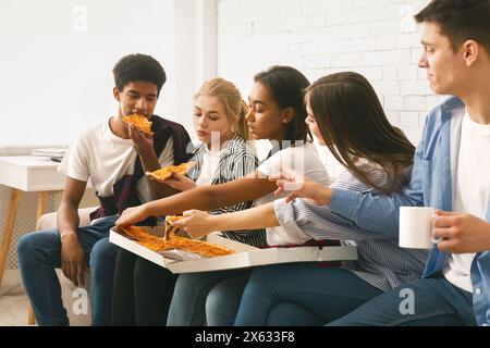 Gruppo di amici che gustano la pizza insieme durante l'incontro informale al coperto Foto Stock