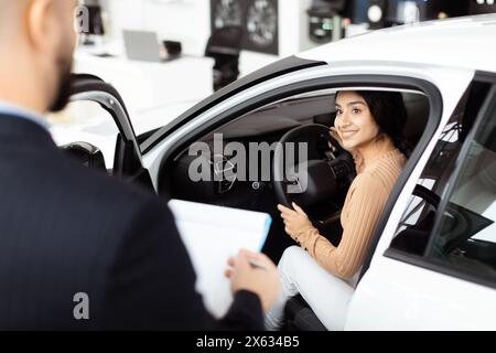 Giovane donna sorridente durante il test di un'auto nuova presso lo showroom della concessionaria Foto Stock