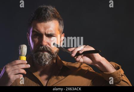 Bell'uomo barbuto con rasoio dritto e spazzola da barba. Accessori per barbiere. Ritratto di barbiere o parrucchiere con barba e baffi con Foto Stock