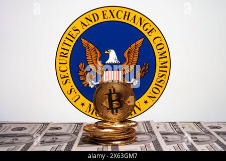 Logo US Securities and Exchange Commission visto sullo schermo e bitcoin con banconote in dollari americani davanti. Stafford, Regno Unito, aprile 28, Foto Stock