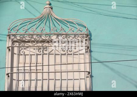 269 il sole del tardo pomeriggio illumina completamente la griglia di una finestra con persiane bianche chiuse in legno, parete verde menta di una casa coloniale. Trinidad-Cuba. Foto Stock