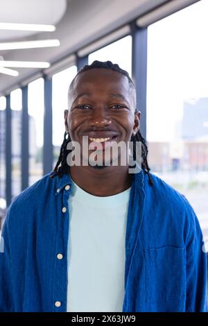 In un ufficio moderno, un giovane afroamericano che indossa un abbigliamento casual e sorride brillantemente Foto Stock