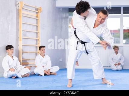 Istruttore di karate maschile che allena un bambino che indossa kimono nel dojo o jiu-jitsu in palestra Foto Stock