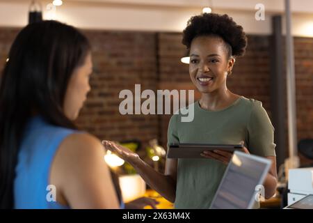In ufficio, diverse colleghe di lavoro condividono un tablet, sorridendo insieme Foto Stock