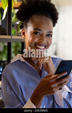 Donna d'affari afroamericana sorridente, con il telefono in mano, lavora fino a tardi Foto Stock