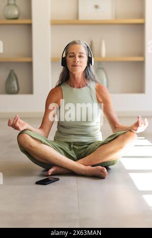 A casa, donna caucasica matura con capelli grigi che meditano con le cuffie Foto Stock