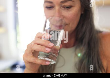 A casa, donna matura caucasica che beve acqua da un bicchiere Foto Stock