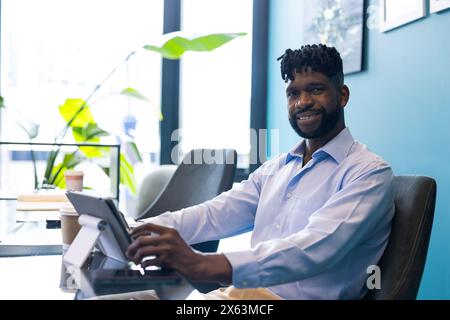 Uomo afroamericano di mezza età che tiene un tablet, sorride alla macchina fotografica in ufficio Foto Stock