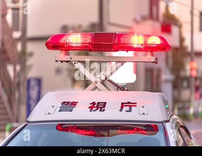 Primo piano sui fari di emergenza rossi brillanti che emettono un'intensa luce mentre si svolgevano sopra il tetto bianco di un veicolo della polizia giapponese che mostra il Foto Stock