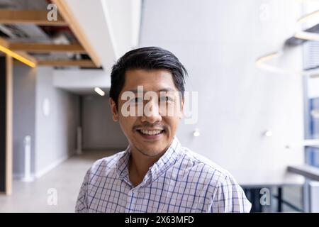 Uomo asiatico professionale in piedi in ufficio, sorridendo alla macchina fotografica Foto Stock