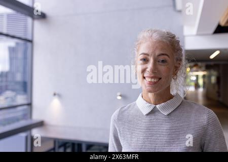 Una donna caucasica di mezza età sorridente in ufficio, in piedi al chiuso, copia spazio Foto Stock
