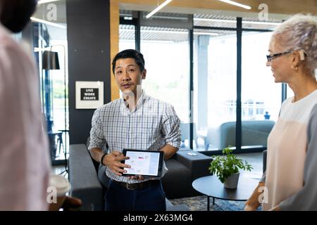 Team diversificato in ufficio che ascolta giovani asiatici con un tablet Foto Stock