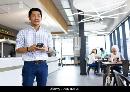 Team diversificato che lavora in ufficio, uomo asiatico che tiene smartphone Foto Stock