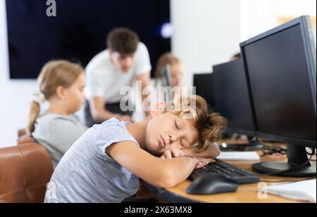 Stanca studentessa maschio si addormentò con la tastiera del computer in classe Foto Stock