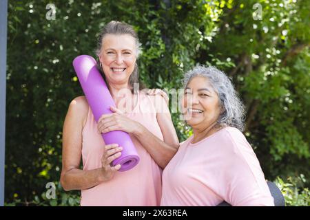 Divertiti all'aria aperta, con diverse amiche anziane che tengono in mano stuoie da yoga, entrambe sorridenti Foto Stock