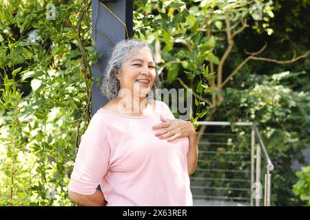 All'aperto, donna birazziale anziana in piedi, mano sul petto, sorridente Foto Stock
