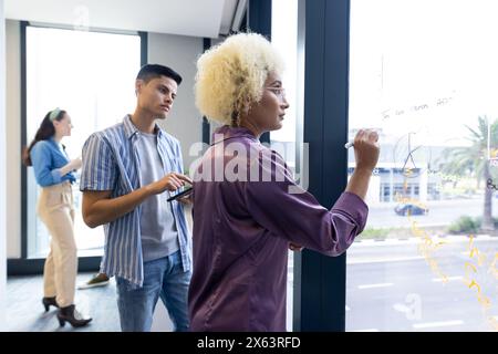 In un ufficio moderno, un team giovane e diversificato che si concentra su una leader birazziale femminile che scrive, copia spazio Foto Stock