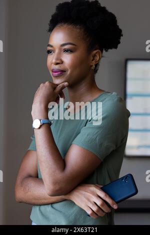In ufficio, donna d'affari afro-americana con smartphone in mano, dall'aspetto premuroso Foto Stock