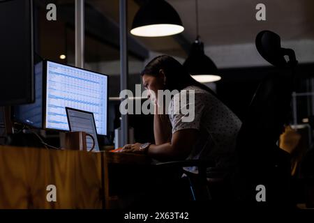 In ufficio, donna d'affari birazziale che esamina il tracker delle vendite, lavora fino a tardi Foto Stock