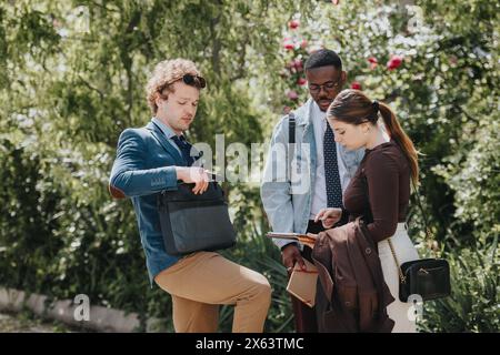 Diversi team aziendali pianificano strategie all'aperto circondati dal verde, analizzando documenti e scambiando idee insieme Foto Stock