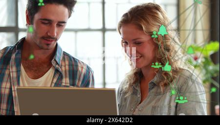 Immagine di due globi di icone digitali contro l'uomo e la donna caucasici sopra un laptop in ufficio Foto Stock