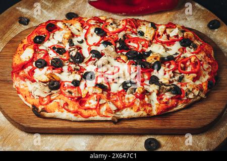 Pizza artigianale con olive e peperoni su tagliere in legno Foto Stock