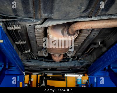 Vista dal basso del tubo di scarico sotto la vettura durante l'intervento di manutenzione di controllo del veicolo sollevato. Una parte del tubo di scarico in metallo presenta macchie di ruggine Foto Stock