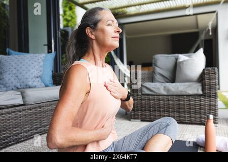 A casa, donna caucasica matura che pratica yoga fuori Foto Stock