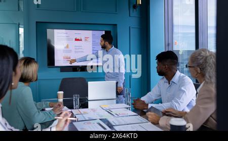 Un team diversificato in ufficio, incluso un uomo birazziale in camicia blu, che punta su uno schermo Foto Stock