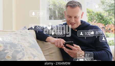 Immagine delle icone dei social media che fluttuano sopra l'uomo caucasico felice che usa lo smartphone a casa Foto Stock