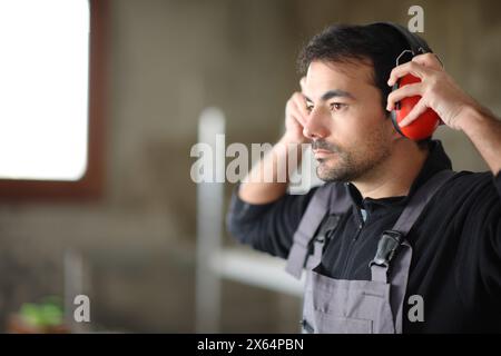 Lavoratore che sta mettendo le cuffie con sistema di cancellazione del rumore in una casa in fase di ristrutturazione Foto Stock