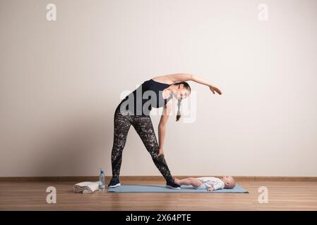 Esercizio domestico per mamma e bambino, mamma e me. Attività fisica per la madre durante il legame con i bambini. Foto Stock