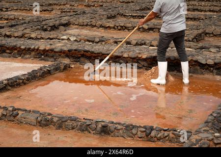 Un uomo sta pulendo una zona fangosa con una pala e una scopa. L'area è piena di rocce e sporcizia, e l'uomo indossa stivali. La scena ha un po' Foto Stock