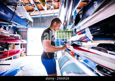 Portrat di giovane canoista in piedi nel mezzo di canoe impilate. Concetto di canoa come sport dinamico e avventuroso Foto Stock