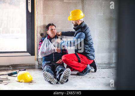 Collega che fornisce il primo soccorso al lavoratore ferito dopo un infortunio in cantiere concetto di sicurezza e salute sul lavoro sul lavoro. Foto Stock