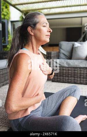 A casa, donna caucasica matura che pratica yoga, seduta seduta a gambe incrociate Foto Stock