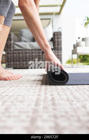 A casa, maturo donna caucasica che rotola fuori stuoia yoga Foto Stock